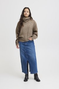 Brun stickad tröja med hög hals, kombinerad med en denimkjol med slits framtill. Svarta ankelstövlar fulländar outfiten.