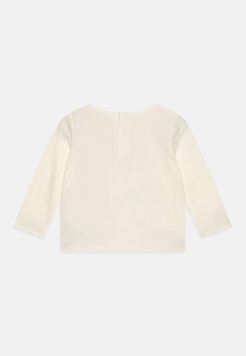 Lange mouwen top in crème katoen met een sluiting aan de achterkant. Zachte, gladde textuur en eenvoudig ontwerp, met een ronde halslijn en gestikte zomen.