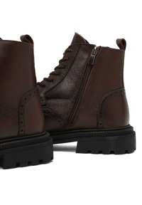 Bottines en cuir brun avec un laçage sur le devant, une fermeture éclair sur le côté, des détails brogués et des semelles en caoutchouc texturé avec un profil résistant.