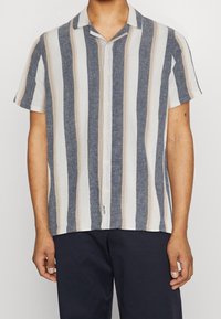 Koszula na krótki rękaw zapinana na guziki w pionowe paski w kolorach granatowym, beżowym i białym, wykonana z lekkiego materiału. Posiada projekt kołnierza typu camp.