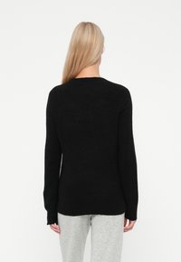 Maglione nero lavorato a maglia con maniche lunghe, colletto rotondo e vestibilità comoda. Tessuto morbido e orlo posteriore leggermente allungato.