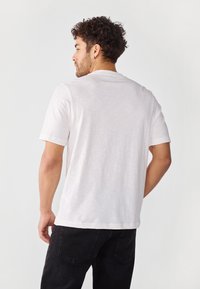 White short-sleeve T-shirt with a crew neck, made of lightweight fabric. Black jeans with a subtle pattern on the back pockets.