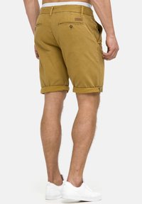 Shorts en khaki avec des ourlets retroussés, deux poches arrière et un petit écusson de marque près de la taille. Texture en coton lisse.