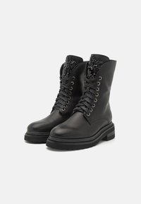 Botas de tobillo negras de piel con cordones, con un acabado suave, una parte superior texturizada y adornos decorativos en el cuello. Suelas de goma gruesas.