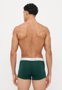 Boxeri scurți din bumbac verde, cu un elastic alb pe care se află textul "TOMMY HILFIGER". Vedere din spate, evidențiind potrivirea și designul.