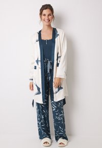 Pigiama blu navy con motivi floreali e un accappatoio bianco con disegni di uccelli. Tessuto morbido e silhouette ampia.