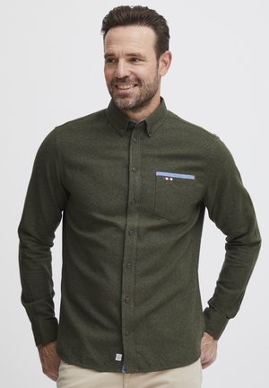 Grønn knapped shirt med en subtil tekstur. Har en brystlomme med blå akcent og logo-tag på nederste kant. Lange ermer.
