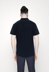 Námořnická košile s krátkým rukávem a límečkem, vyrobená z hladkého materiálu se rovním lemem, v kombinaci s pruhovanými kalhotami.