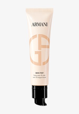 Beige plastic tube with a black pump dispenser. Features "Armani" logo and "Skin Tint" label in black. Smooth texture with subtle sheen.