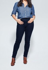 Granatowe dżinsowe rurki w połączeniu z jasnoniebieską dżinsową koszulą. Całość uzupełniają wzorzyste brązowe botki za kostkę.