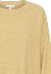 Maglione giallo a maglia con scollatura circolare, texture morbida e spalle basse. L'etichetta mostra il nome del marchio e la taglia "S".