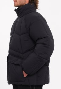 Zwarte pufferjack met hoge kraag, ritssluiting, voorzakken met drukknoopsluitingen en een doorgestikt ontwerp voor isolatie en warmte.