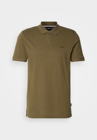 Polo vert olive en coton, présentant une patte à deux boutons, des manches courtes et un logo discret sur la poitrine. Design basique avec fentes latérales.