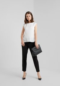 Haut blanc en soie avec des manches courtes, associé à un pantalon noir cintré. Tient un sac à main en cuir noir et porte des escarpins noirs à bout pointu.