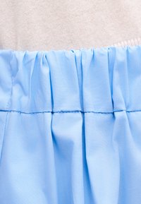 Ανοιχτό γαλάζιο ύφασμα μαζεμένο με ελαστική ραφή πάνω, προσαρτημένο σε απαλό ροζ πλεκτό ύφασμα.