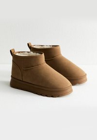 Botas tobilleras marrones hechas de un material suave y texturizado con un forro acolchado. Cuentan con una punta redondeada y una suela de goma con dibujo para mayor agarre.