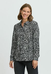 Camicia a righe in bianco e nero con collo e maniche lunghe, realizzata in un tessuto leggero. Abbinata a jeans scuri.