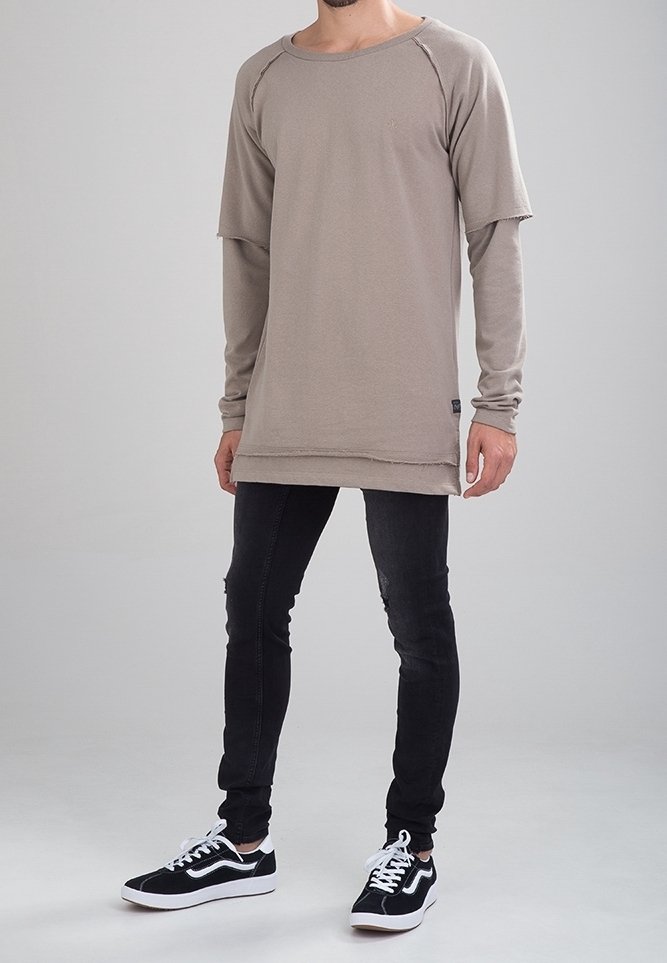 Camisa de manga larga beige con escote redondo y bordes sin terminar, combinada con jeans ajustados negros y zapatillas negras con detalles blancos.