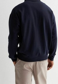 Sudadera azul marino de manga larga, con cuello redondo y puños y dobladillo acanalados. Fabricada en un tejido suave, sin patrones visibles.