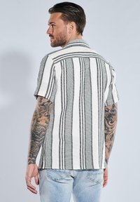 Kurzärmliges Hemd mit Knöpfen, das ein gestreiftes Muster in Schwarz und Weiß aufweist, mit einer gewebten Textur und einem Kragen.