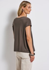 Haut marron à manches courtes avec une coupe décontractée, une texture lisse et un col rond. Associé à un pantalon de couleur claire et à des bracelets jonc.