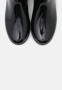 Bottines noires brillantes avec une texture lisse, des bouts ronds et sans aucune quincaillerie visible. Des coutures droites bordent le centre de chaque bottine.