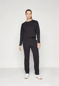 Sweat-shirt noir et pantalon assorti en tissu doux ; coupe décontractée avec un col rond ; le mannequin porte des baskets blanches ; design minimaliste.