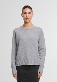 Grauer Strickpullover mit rundem Halsausschnitt, geripptem Saum und langen Ärmeln. Das Material hat eine weiche Textur und ein leicht lockeres Design.