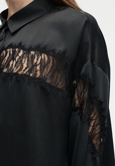Μαύρη σατέν μπλούζα με διάφανο μαύρο δαντελένιο πάνελ στο στήθος και στα μανίκια, με γιακά και κούμπωμα με κουμπιά.