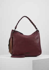 Sac à main en cuir bordeaux avec une texture granuleuse, poignée tressée et détail en pompon. Doté d'une bandoulière amovible et de quincaillerie en métal.