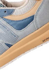 Gros plan d'une basket bleue et beige montrant des textures mixtes en tissu et en suède avec le texte "WORKS OF DENMARK" sur le côté et une semelle rembourrée.