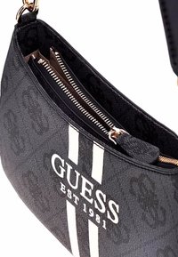 Borsa a tracolla nera in tessuto con un motivo testurizzato, caratterizzata da righe bianche e un logo "GUESS EST 1981". Include scomparti con cerniera.