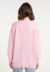 Suéter de punto de gran tamaño en rosa claro, con un cuello alto y un patrón moteado texturizado; cuenta con mangas ajustadas y un dobladillo acanalado.