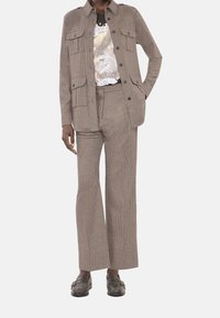 Brązowa kurtka w kratę z czterema przednimi kieszeniami, w połączeniu z szerokimi spodniami w tym samym wzorze. Pod spodem T-shirt z graficznym nadrukiem. Całość dopełniają ciemne loafersy.