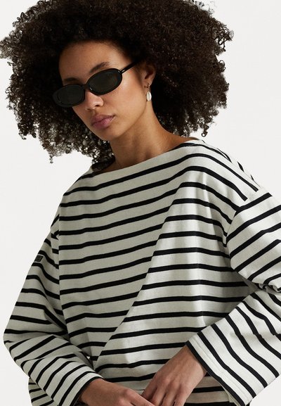 T-shirt surdimensionné rayé gris et noir, avec un col bateau, des manches longues et une texture côtelée. Accompagné de lunettes de soleil sombres.
