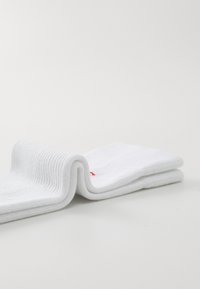 Hvite bomullssokker med ribbestruktur, brettet i to. Har en liten rød detalj. Stoffet ser mykt og lett ut.