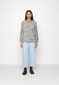 Blusa floreale con maniche lunghe, chiusura a bottoni e dettagli verdi. Abbinata a pantaloni larghi azzurri e stivaletti neri.