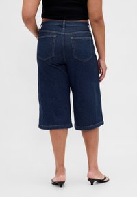 Denim culottes i mörkblått med avslappnad passform, knälång skärning och traditionell femficksdesign. Har midjeband med bälteshällor.