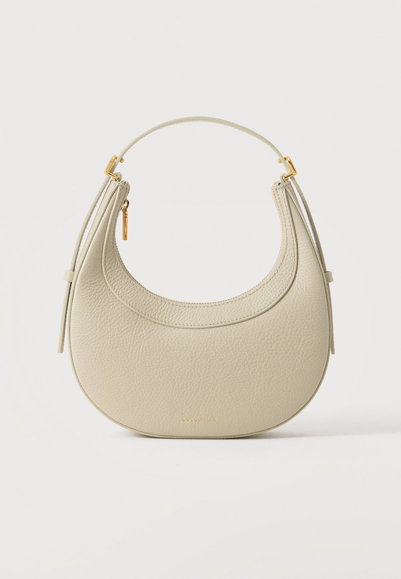 Sac à main en cuir texturé couleur crème en forme de croissant avec une petite poignée, tirette de fermeture éclair dorée et nom de marque embossé subtil en bas au centre.