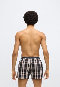 Fekete kockás boxeralsó bézs és fehér csíkokkal. Látható elasztikus derékpánt. A személy hátulról látható, ing nélküli. Simább bőrfelület.