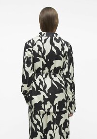 Chaqueta de estampado en blanco y negro con un corte holgado, que cuenta con un cinturón en la cintura y mangas largas, vista desde la parte de atrás.