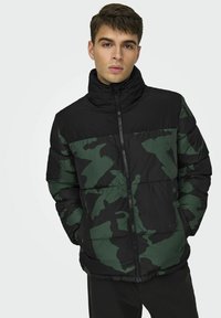 Giacca a puffo camouflage nera e verde con colletto alto e chiusura con zip, caratterizzata da pannelli cuciti e una texture lucida.