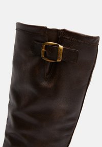 Brown leather knee-high boot with a textured finish, featuring a brass buckle accent on the side and a stitched seam along the top edge.