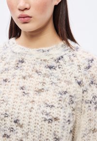 Leichter, flauschiger Pullover mit einem cremefarbenen Grundton und dezenten blauen und braunen Sprenkeln. Gestrickte Textur und ein runder Halsausschnitt.