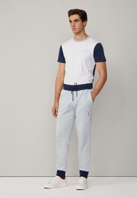 Witte en marineblauwe crew neck t-shirt met logo, gecombineerd met grijze joggers met een trekkoord en marineblauwe manchetten. Witte sneakers maken de look compleet.