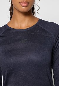 Granatowa sportowa koszulka z długim rękawem, wykonana z teksturowanej tkaniny, z okrągłym dekoltem i subtelnym logo na klatce piersiowej.