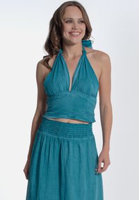 Top corto halter turchese con scollo arricciato e spalline da legare, abbinato a una gonna smock coordinata con una silhouette fluida.