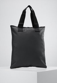 Sac fourre-tout noir en matériau lisse et durable. Forme rectangulaire avec deux poignées en tissu robustes. Design minimaliste, sans éléments métalliques visibles.