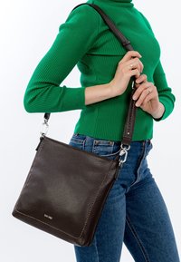 Brun skuldertaske i læder med en glat tekstur, firkantet form og kontrastsyet, med aftagelig rem og metalhardware-detaljer.