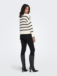 Randig tröja i krämvitt och svart, oversize passform, med långa ärmar. Kombinerad med svarta tajta jeans och knähöga svarta stövlar med klack.